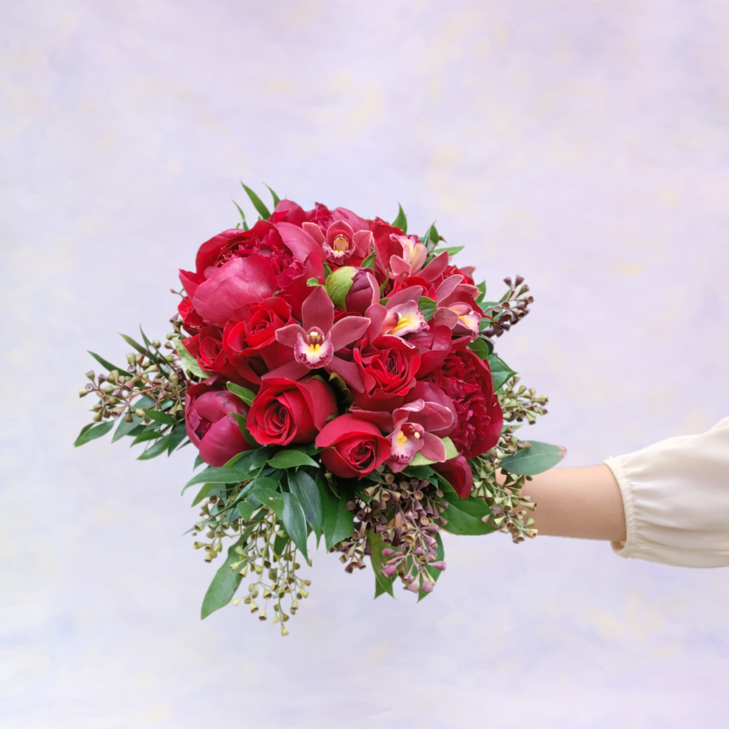 Bouquet of red and pink flowers held by a person against a light purple background