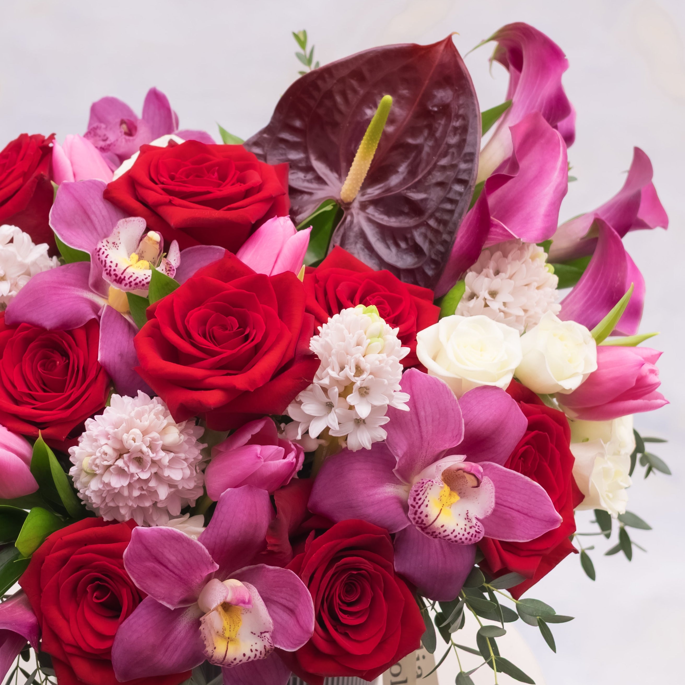Close-up of Devotion arrangement featuring red roses, pink orchids, and burgundy anthuriums by Niolia, San Francisco florist