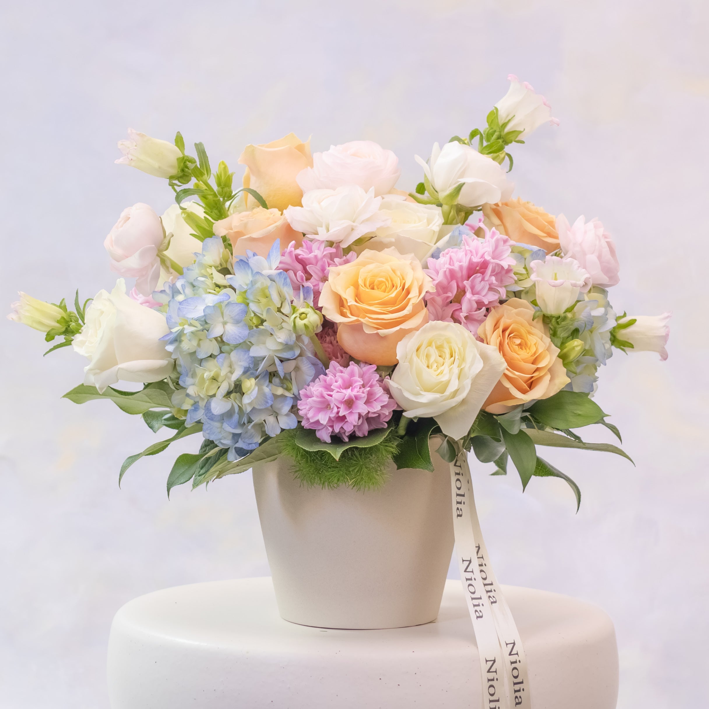 Pastel flower arrangement in a white pot on a light gray background