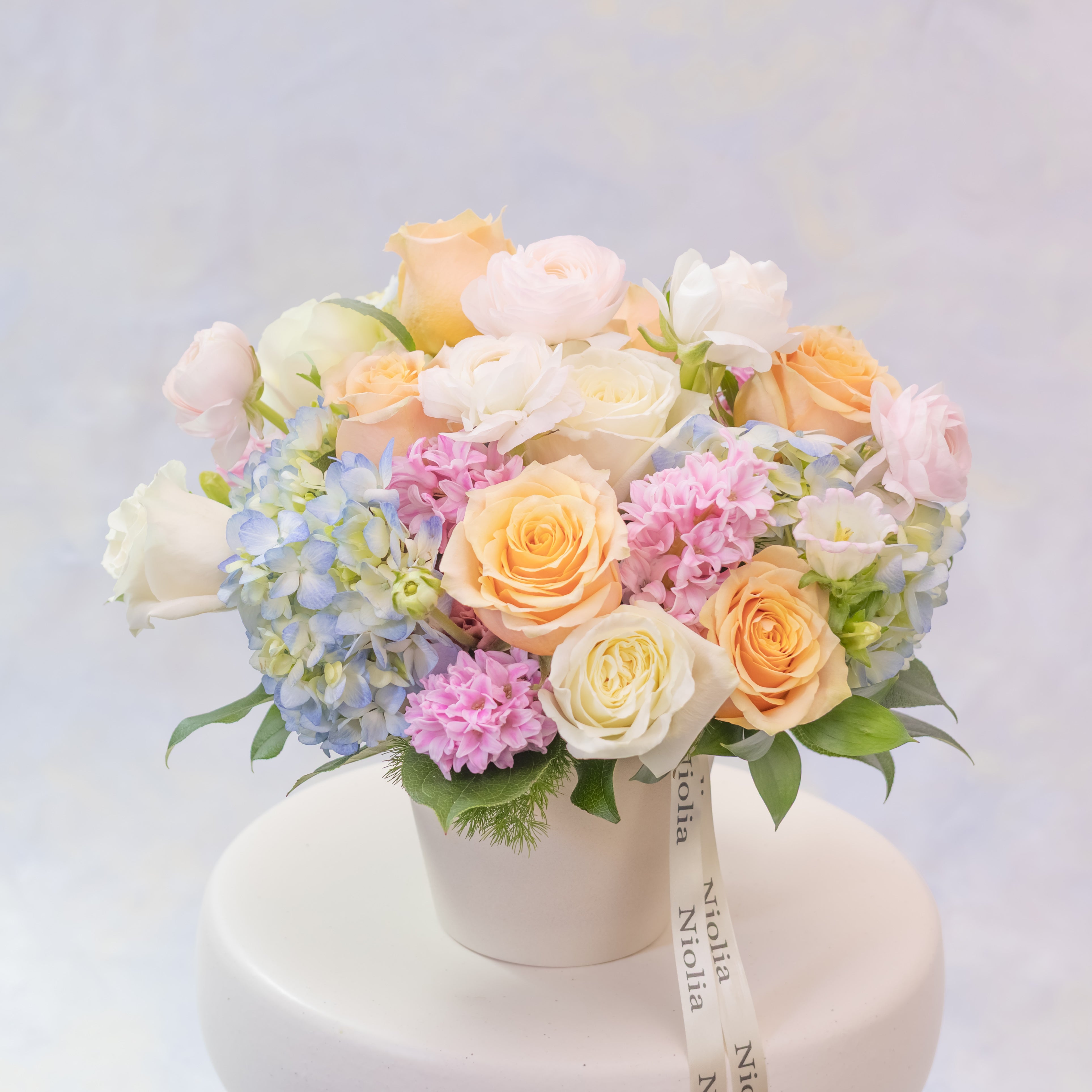 Pastel-colored flower arrangement in a white box on a light gray background