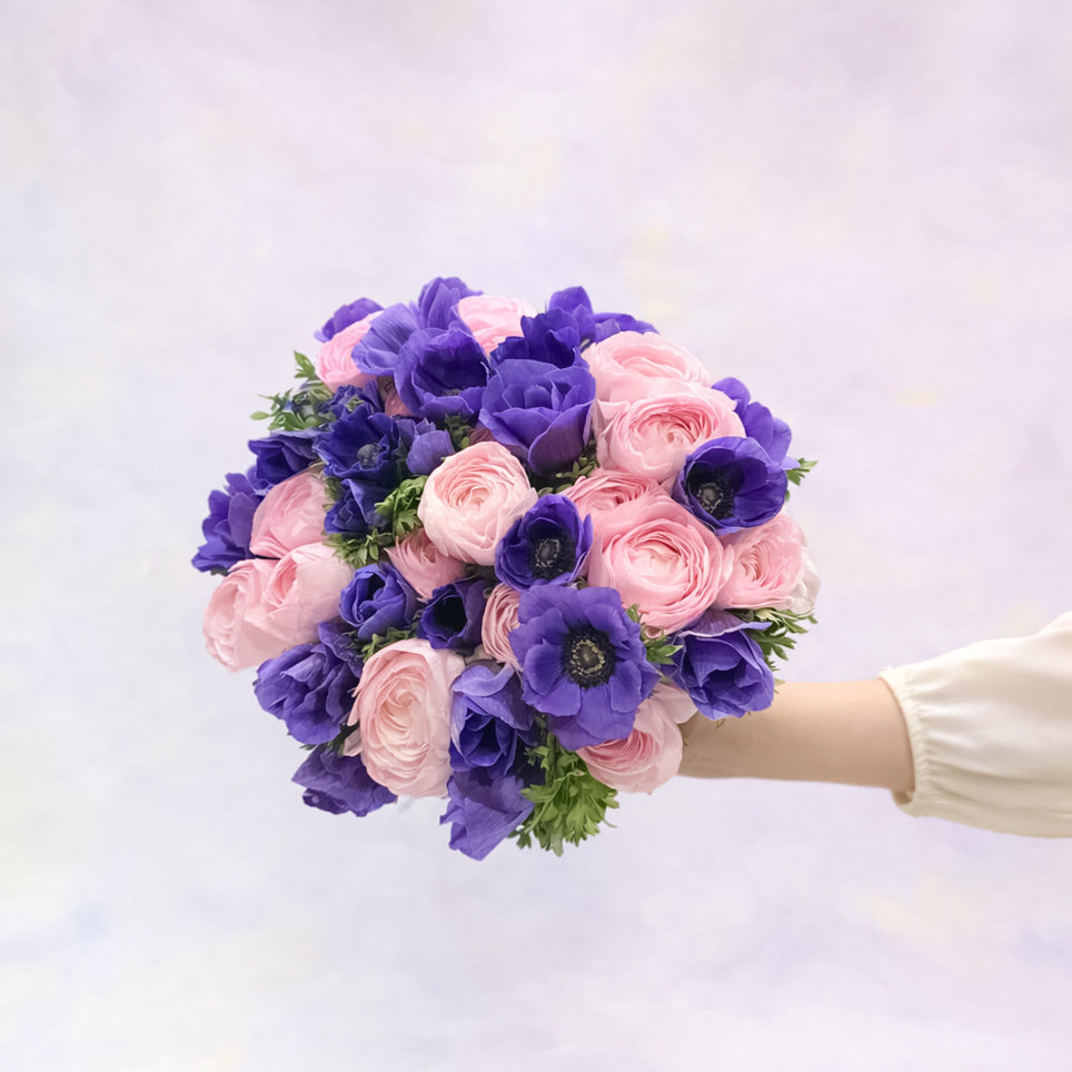 Bouquet of pink and purple flowers held by a person against a light background