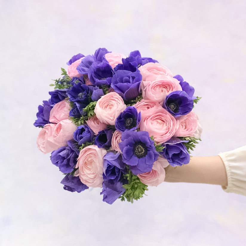 Bouquet of pink and purple flowers held by a person on a white background